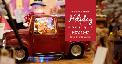 Festive holiday scene with a miniature red truck holding a snow globe featuring Santa Claus, surrounded by holiday decorations. A graphic overlay on the right reads 'Des Moines Holiday Boutique, Nov. 15-17, Iowa Events Center,' in white and gold text on a red background.